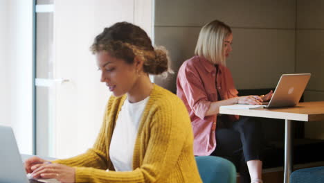 dos mujeres creativas del milenio sentadas en una oficina trabajando en computadoras, enfoque selectivo