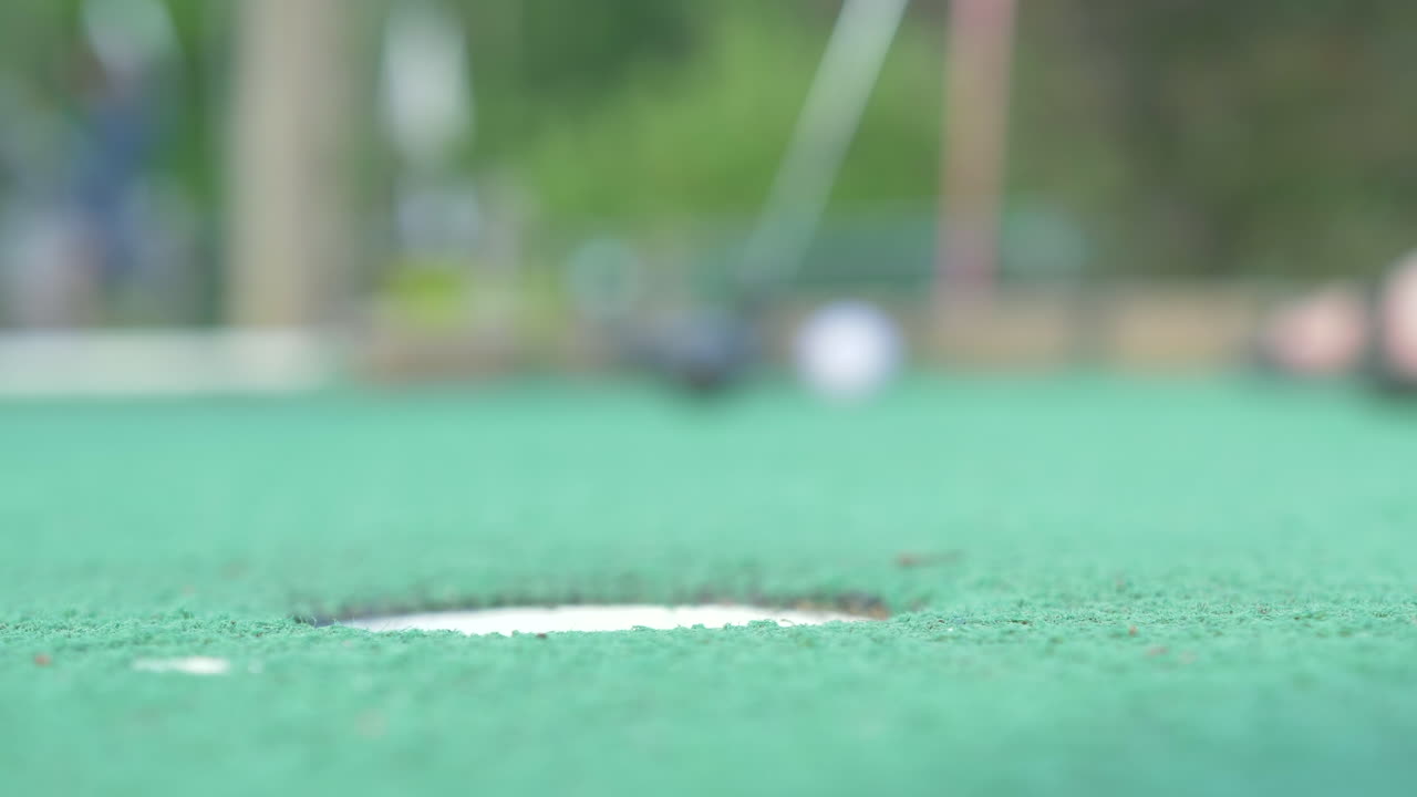 A Mini Golf Player Putts and Gets the Golf Ball in the Hole, Low Angle Slow Motion, Shallow Depth of Field