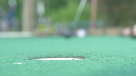 un jugador de mini golf pone y consigue la pelota de golf en el agujero, ángulo bajo movimiento lento, profundidad de campo poco profunda
