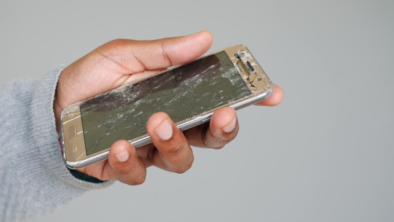Nærbillede af en hånd der holder en smartphone med en alvorligt revnet skærm