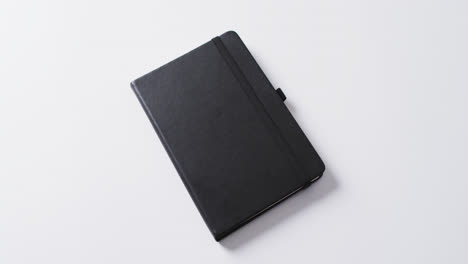 Close-up-of-closed-black-notebook-with-copy-space-on-white-background-in-slow-motion