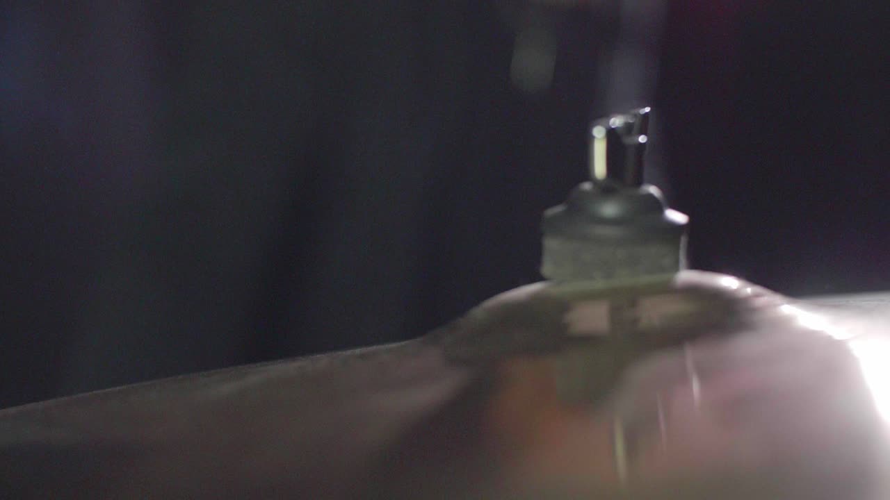 Smooth close up of a drum crash cymbal being hit with a stick. Cymbal wobbling afterwards. Dark Background. Super slow motion. Dolly Gimbal backwards movement. Shallow depth with fixed focus