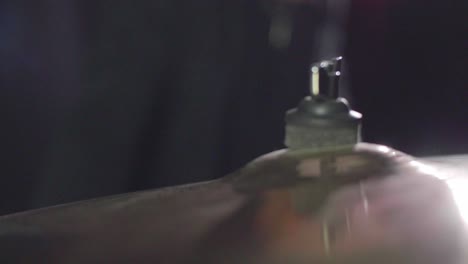 smooth close up of a drum crash cymbal being hit with a stick. cymbal wobbling afterwards. dark background. super slow motion. dolly gimbal backwards movement. shallow depth with fixed focus