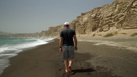siguiendo a un hombre que camina descalzo en la playa de vlychada
