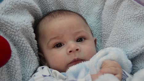 cute-tree-months-old-baby-boy-making-funny-faces-in-baby-bouncer-on-light-blue-blanket