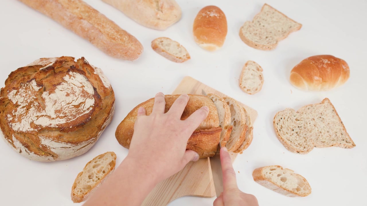 Overhead shot of hands using a knife to slice crusty sourdough bread on white background.