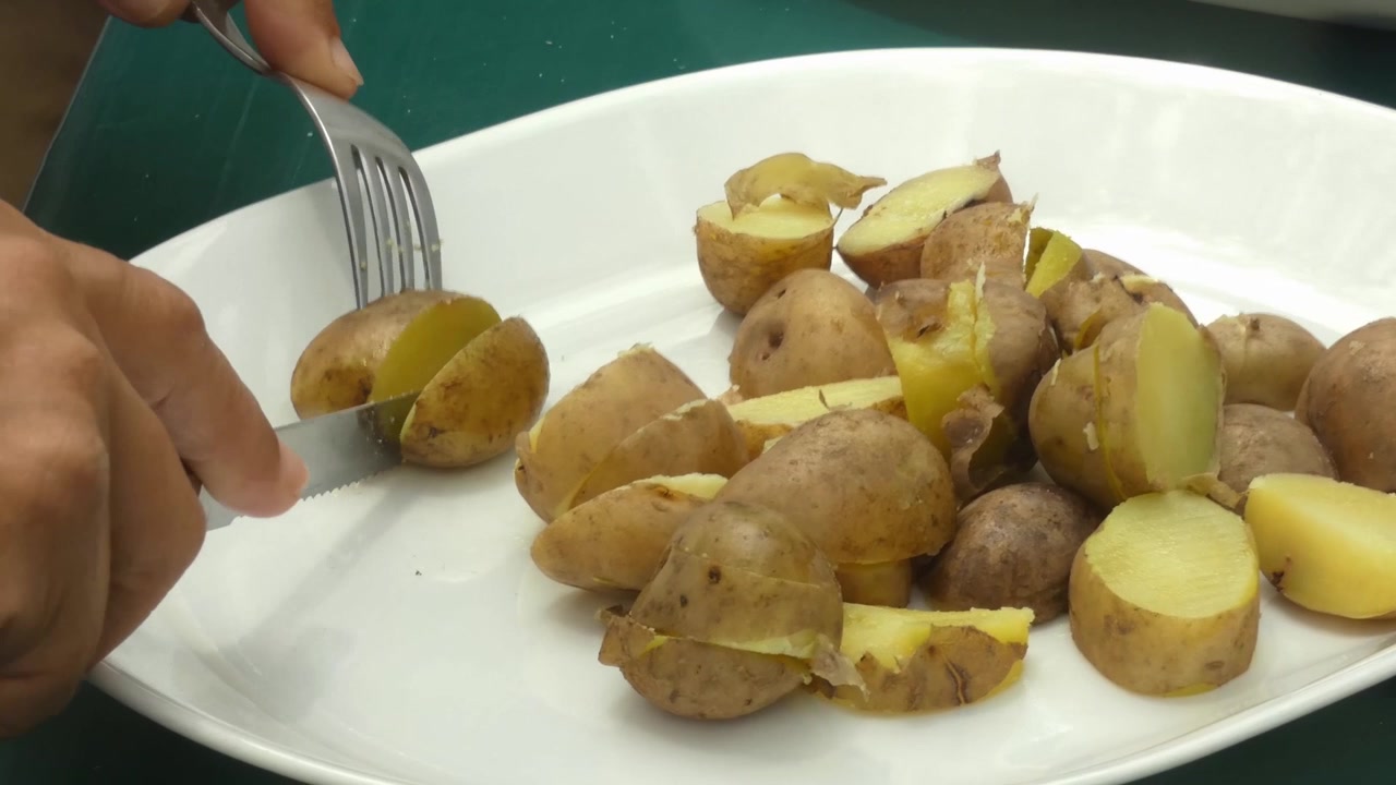 Tagliare piccole patate peruviane gialle bollite su un piatto, con un coltello e una forchetta
