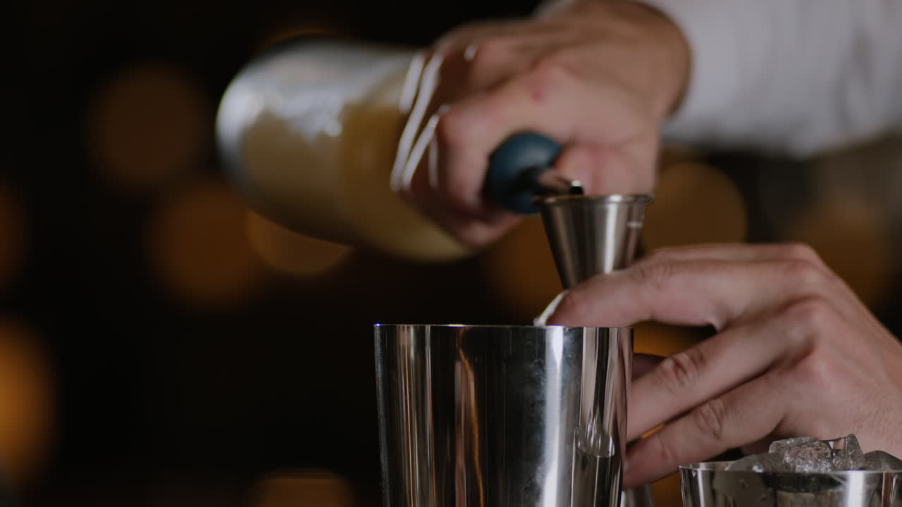 fotografía de primer plano de un camarero midiendo licor en un jigger y vertiéndolo en un agitador de metal