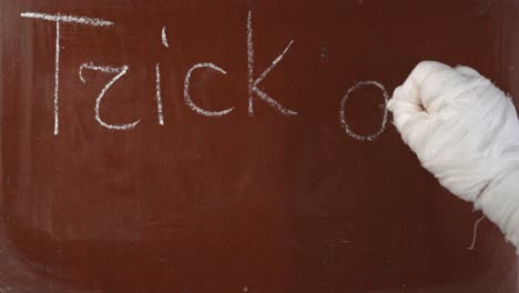 textured brown chalkboard background mummy's hand in bandages writing 'mummy' on the board with a