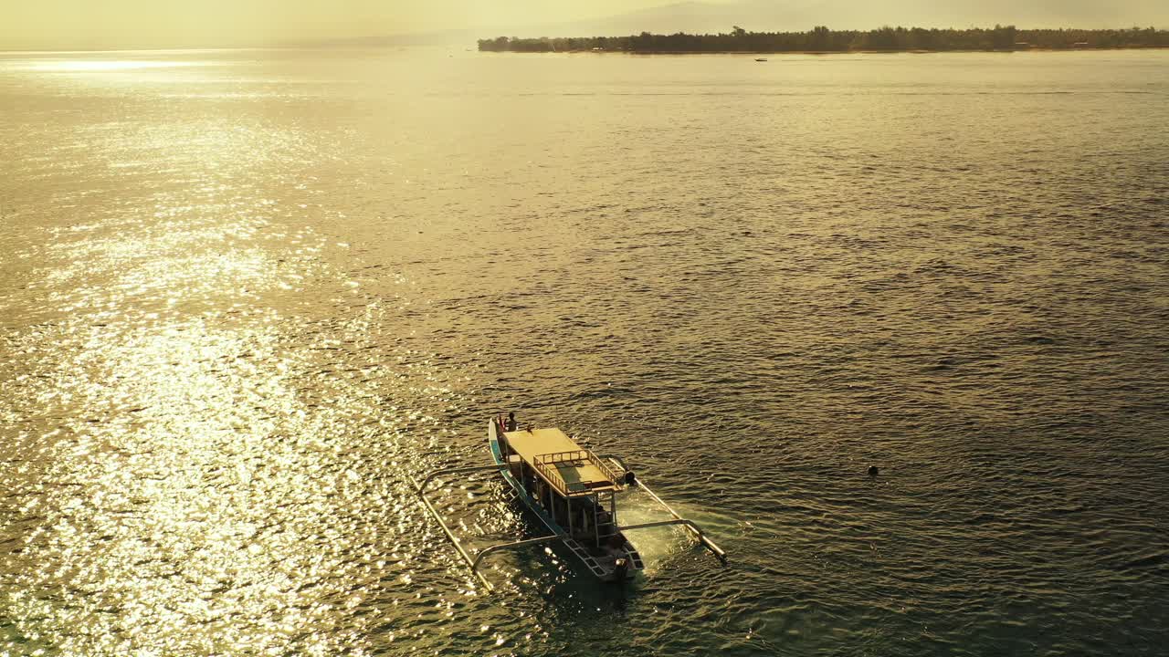 barco indonesio navegando en la tranquila laguna brillante por la luz del sol reflejada por la hermosa puesta de sol en bali