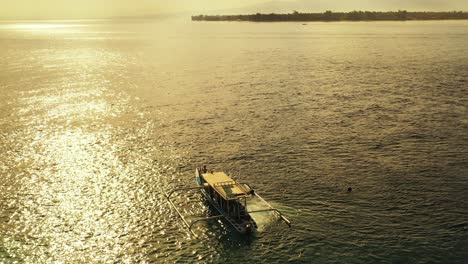 Indonesisches-Boot-Segelt-Auf-Einer-Ruhigen,-Leuchtenden-Lagune-Im-Sonnenlicht,-Das-Vom-Wunderschönen-Sonnenuntergang-Auf-Bali-Reflektiert-Wird