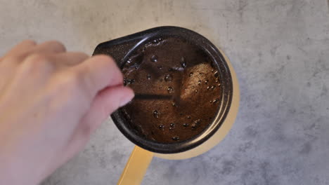 Female-hand-making-and-stirring-dark-coffee-in-coffee-cooking-pot-before-boiling-it-on-stove-in-50-fps