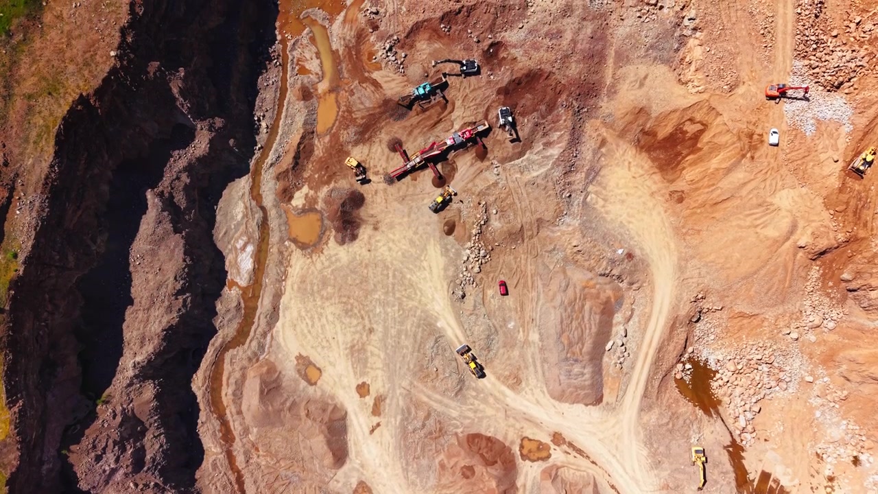 Aerial view of quarry pit floor with dirt roads and machinery. Loader, excavator and muddy pools among rock walls.