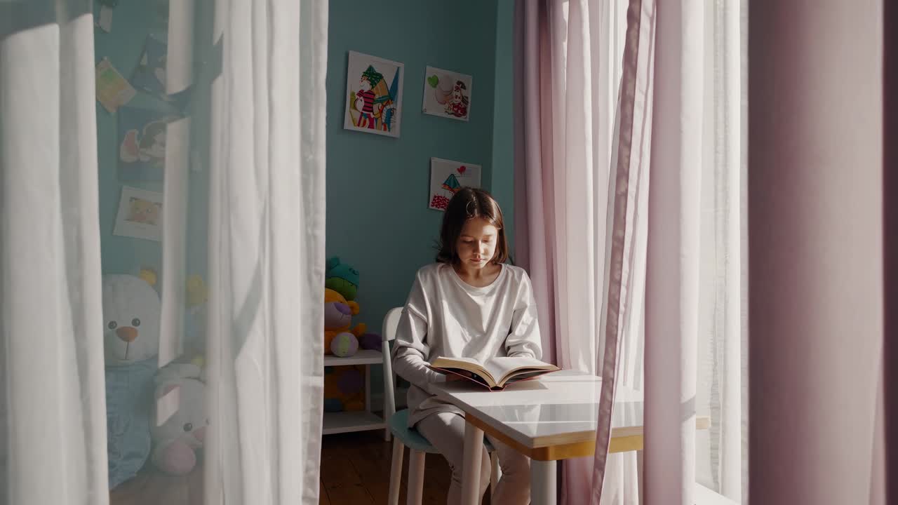 A young girl sits in a colorful room with toys and pictures, captured in a video from a low angle