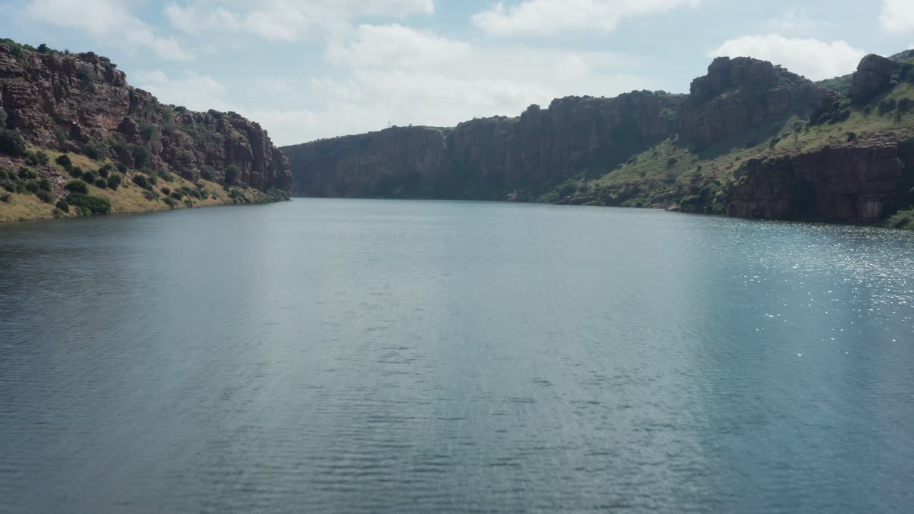Low-altitude drone captures Pennar River reservoir stretching between Gandikota Canyon's towering red rock walls and green canyon rims under partly cloudy skies