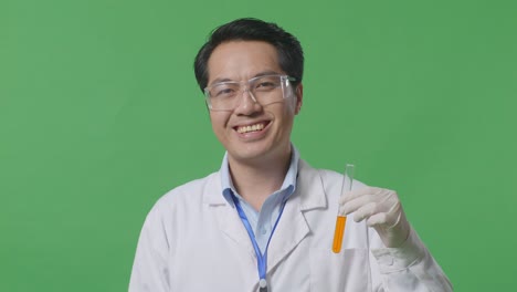 close up of asian man scientist smiling and showing orange liquid in the test tube to camera while standing on the green screen background in the laboratory