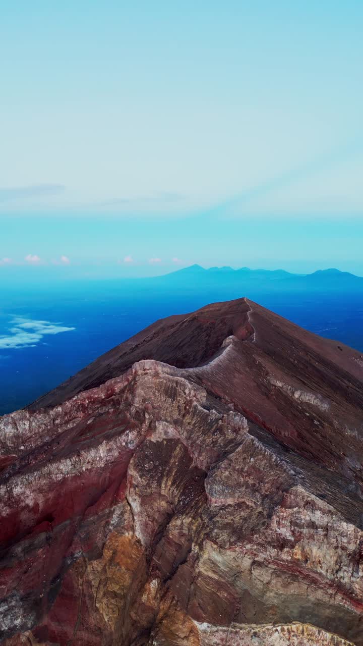 Vertical aerial footage shows the dramatic landscape of Mount Agung volcano with its sharp crater edges and sweeping views that unfold slowly as the drone ascends above the summit.
