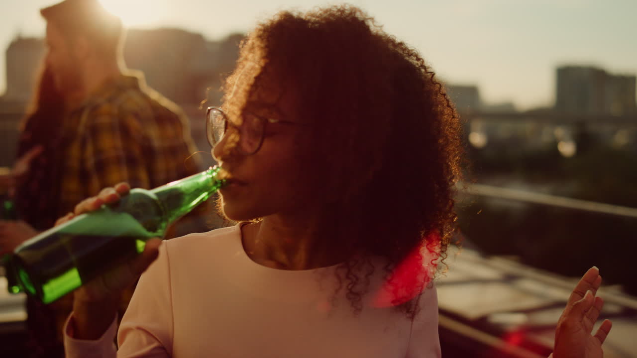 African girl drinking beer at party. Happy woman having drink at sunset disco.