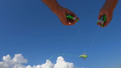 low angle pov of male hands controlling flying green kite high up in blue sky holding green reels