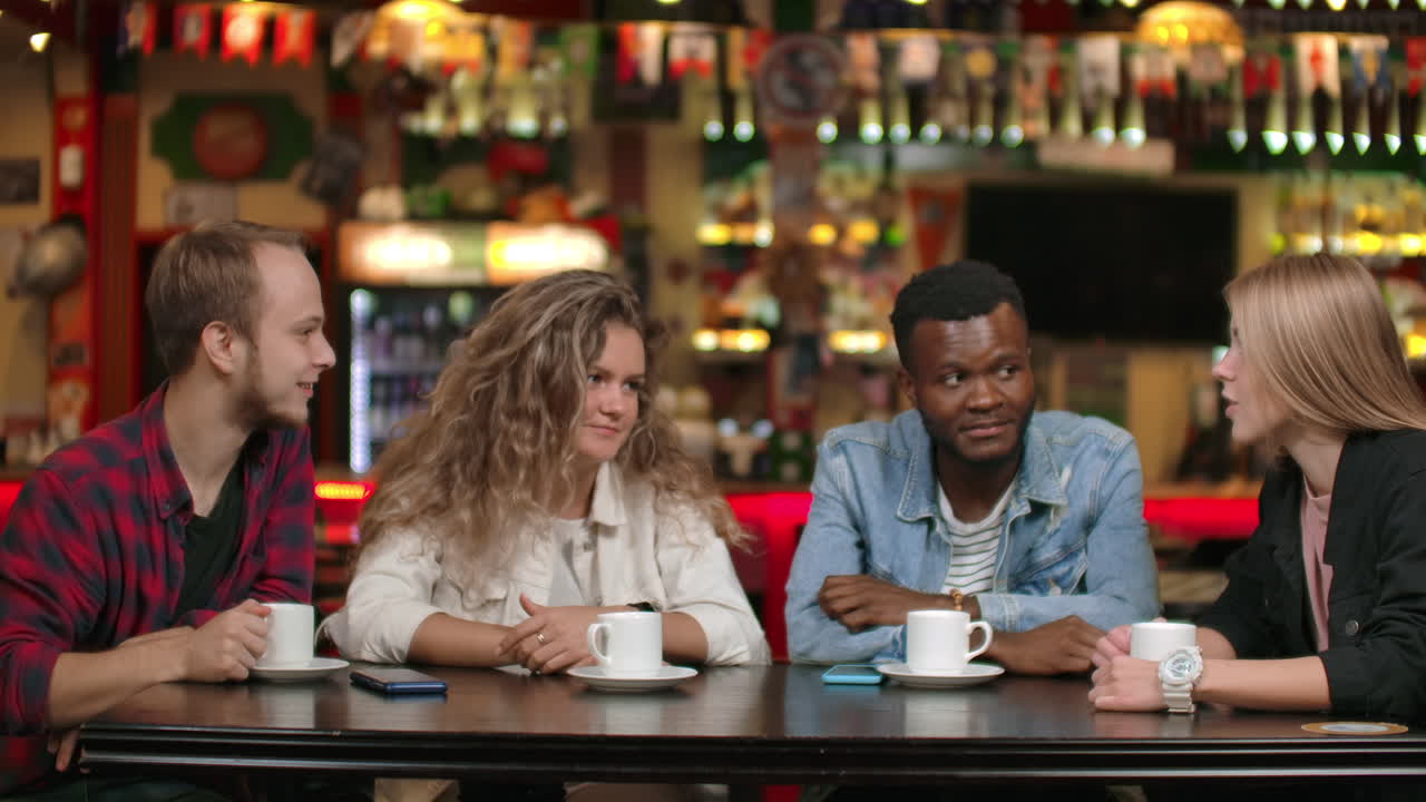 친구들의 다국적 회사가 레스토랑에서 커피를 마시며 대화하고 있습니다. 네 명의 친구가 대화하고 있어요.