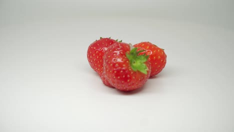 three delicious and fresh strawberries on the rotating table with pure white background - close up shot