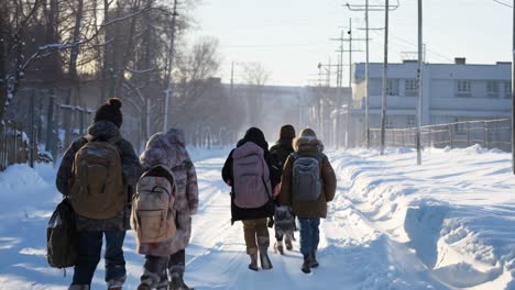 students walking together on snow covered rural road, carrying backpacks during cold winter afternoon with soft sunlight filtering through distant trees