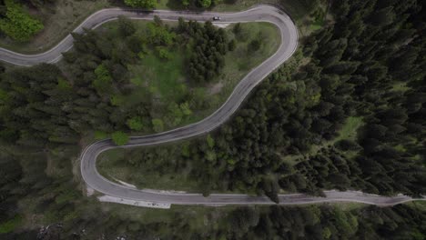 Top-down-aerial-car-driving-on-a-winding-road-through-a-green-forest