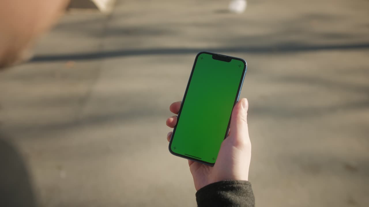 Young man holding phone chroma key screen on the street close-up. Male with green screen on smart phone swiping .