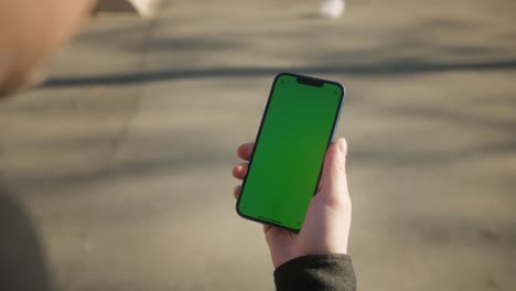 young man holding phone chroma key screen on the street close-up. male with green screen on smart phone swiping .