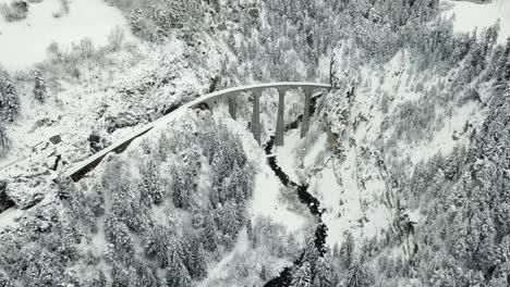 drone view of the landwasser viaduct, a stunning railway bridge amidst a snowy forest landscape, flying forward cinematically