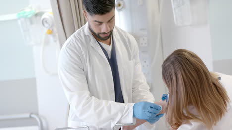 Focused-diverse-male-doctor-taking-blood-sample-from-girl-patient-in-bed-with-syringe,-slow-motion