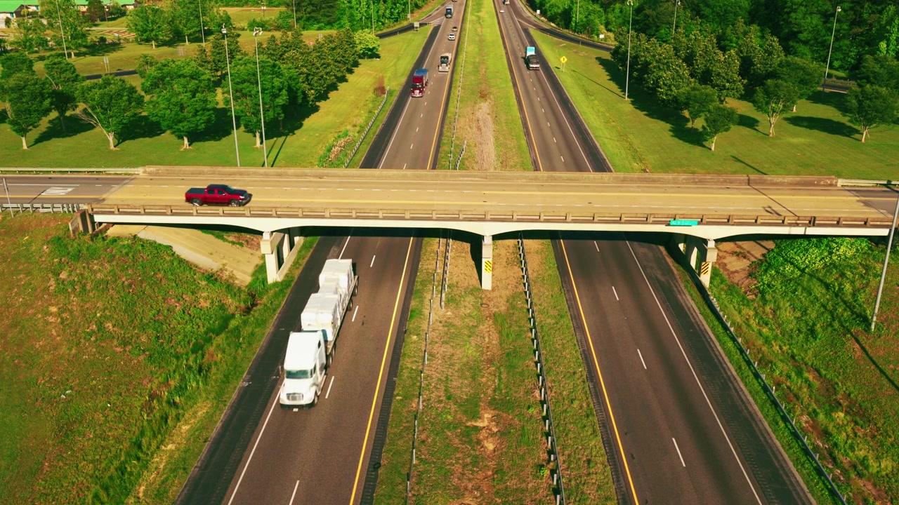 Semirimorchio a pianale con un carico telonato e fissato che percorre un'autostrada divisa verso un cavalcavia in cemento, con traffico leggero e spartitraffico verdi negli Stati Uniti meridionali