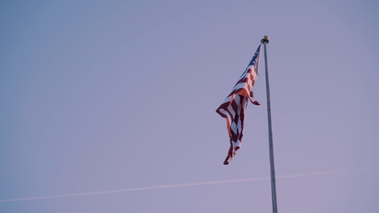 bandera estadounidense en lo alto de un poste soplando en el viento