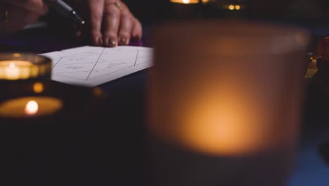 primer plano de una mujer dibujando astrología lagna o carta natal en la mesa a la luz de las velas 8