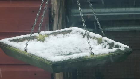 comedero para pájaros cubierto de nieve fría y vacía colgando de una cadena durante las nevadas