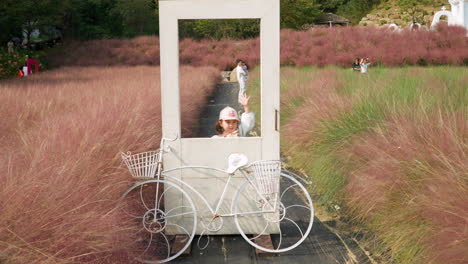 child girl pose at photo zone with pink muhly grass by white door and bicycle in herb island pochen