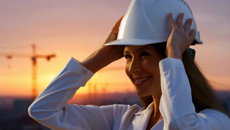 female engineer puts on hard hat against sunset sky