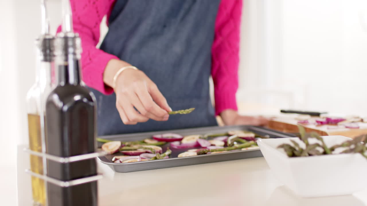 sección media de una mujer biracial preparando comida en la cocina en casa con espacio de copia, cámara lenta