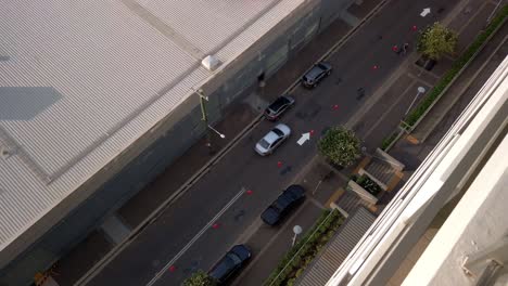 top down view of a small street between two small buildings with people walking, car crossing and parking.