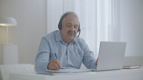 aged man is working from home using notebook for communicating with colleagues and partners making notes on paper