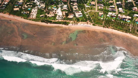 Vista-Aérea-De-La-Playa-Praia-Do-Forte,-El-Arrecife-De-Coral,-La-Zona-De-Palmeras-Y-La-Ciudad-Circundante,-En-Un-Día-Nublado,-Praia-Do-Forte,-Bahia,-Brasil