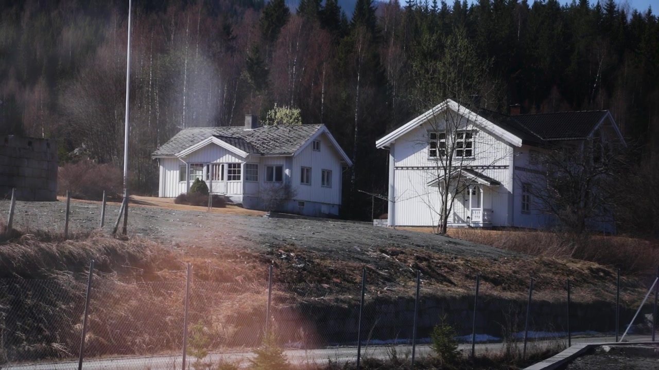 To hvide landhuse på en bakkeskråning med skov i baggrunden i forårssolskin, Norge, Europa.