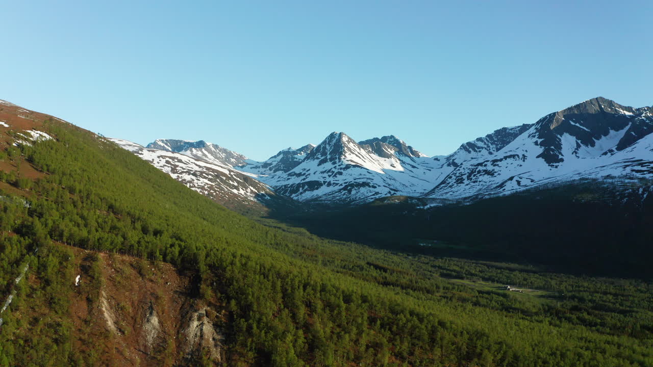 vista aérea con vistas a los árboles y la naturaleza, hacia los picos de las montañas nevadas, un día soleado de verano, en los alpes de lyngen, norte de noruega - descendiendo, disparo de drones