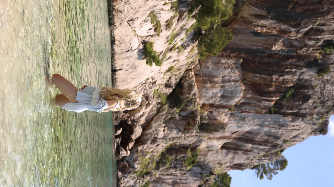 mujer rubia embarazada en aguas poco profundas de la playa de nugal cerca del acantilado costero, vertical