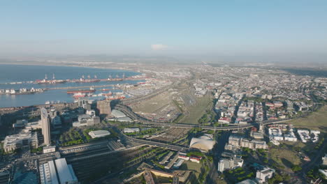 Aerial-panoramic-shot-of-transport-infrastructure-in-large-city.-View-of-big-oversea-harbour,-train-station-with-extensive-rail-tracks-and-busy-trunk-roads.-Cape-Town,-South-Africa