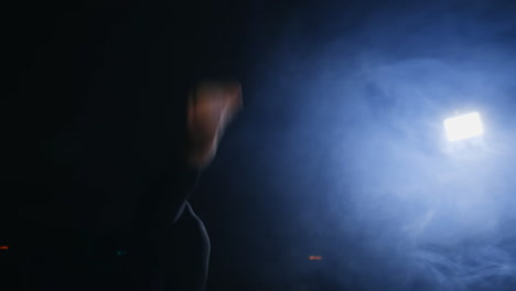 Girl-gymnast-performs-flips-on-the-gymnastics-carpet-in-slow-motion-in-the-back-light-in-the-smoke