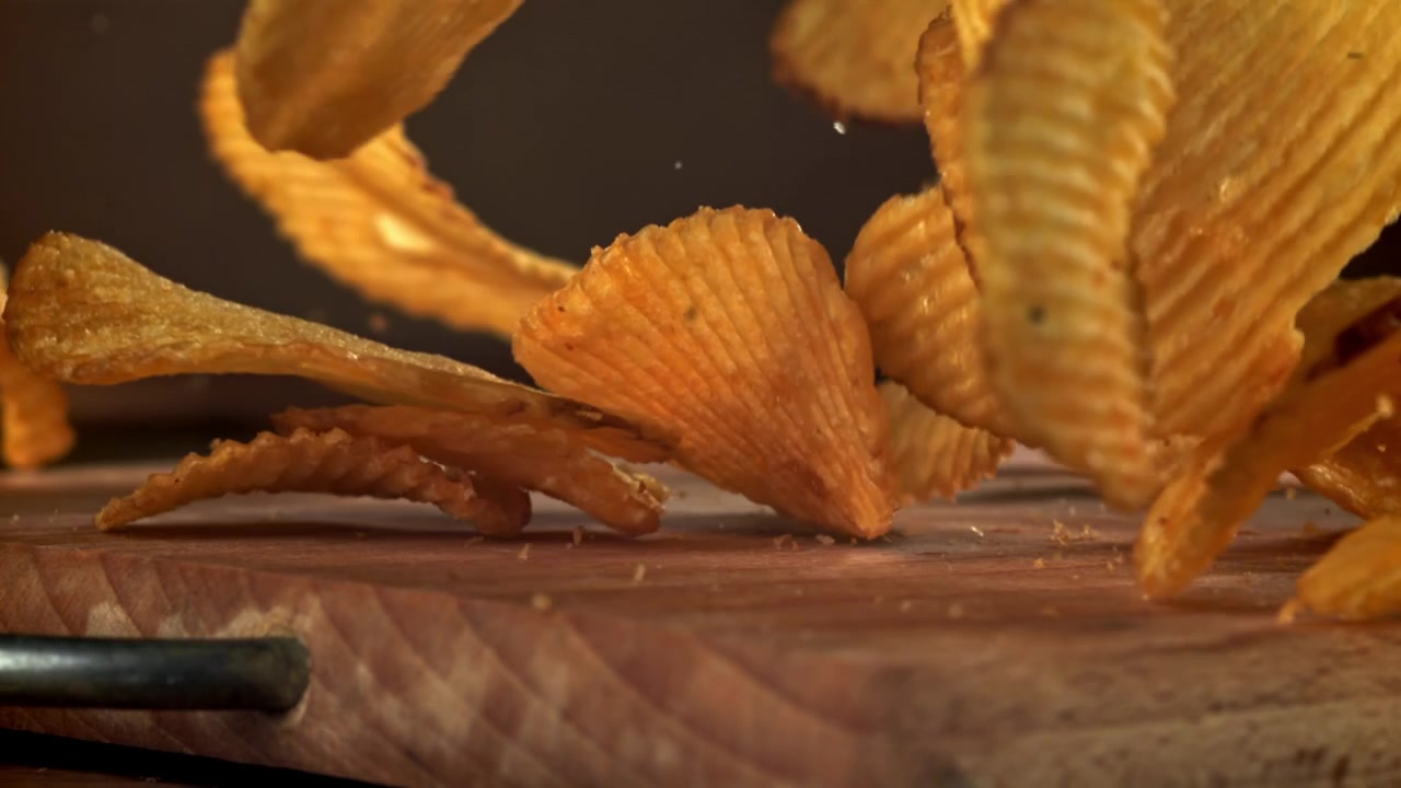 Slow Motion of Crispy Corrugated Potato Chips Falling onto a Wooden Board