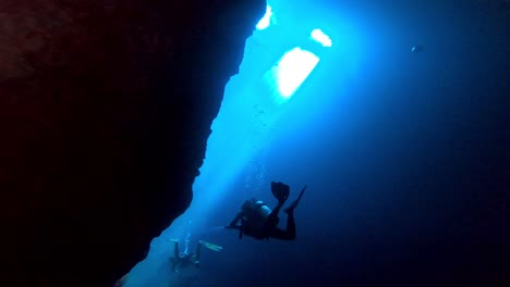 scuba diver swimming in a underwater cave with sun beams in the background