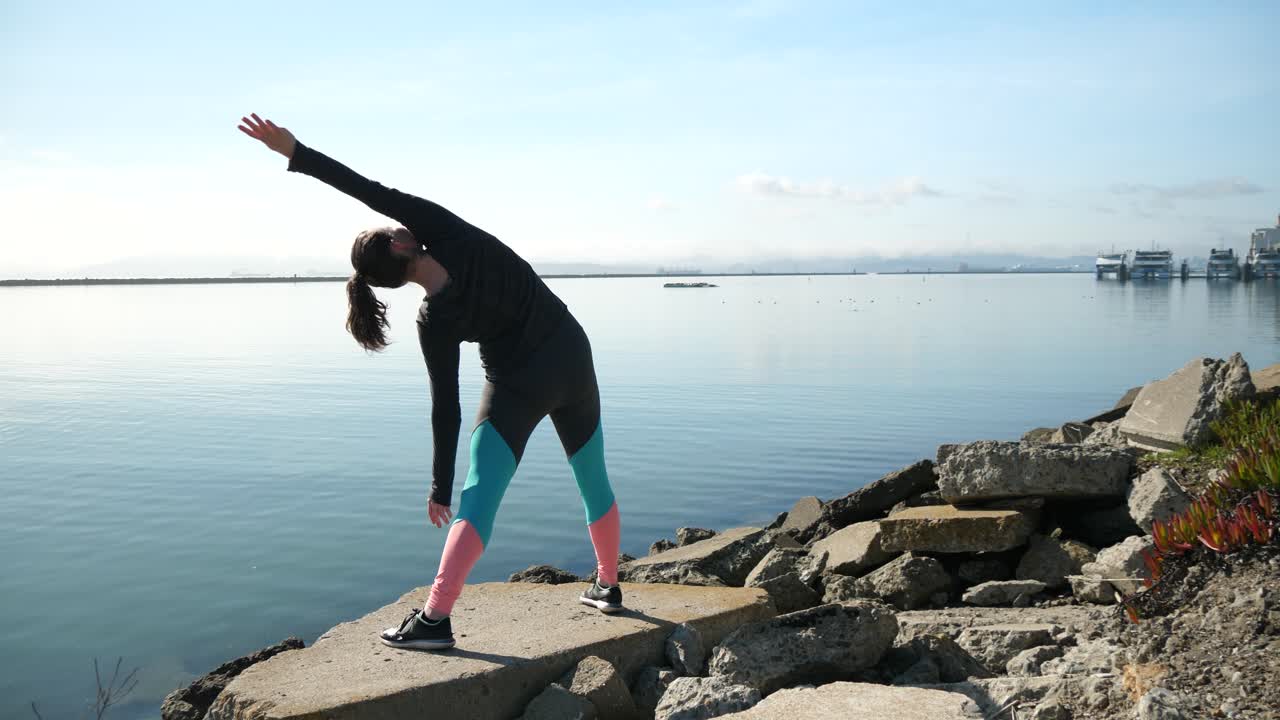 A girl stretching on the shoreline looking out into the San Franciso Bay while balancing on a rock.