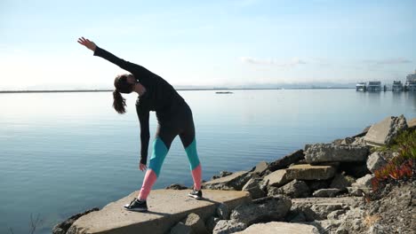 a girl stretching on the shoreline looking out into the san franciso bay while balancing on a rock.